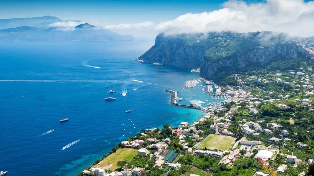 Vue aérienne de Capri, une île près de Naples, avec son port animé, des bateaux naviguant sur la mer bleue et des maisons blanches nichées sur les collines verdoyantes.