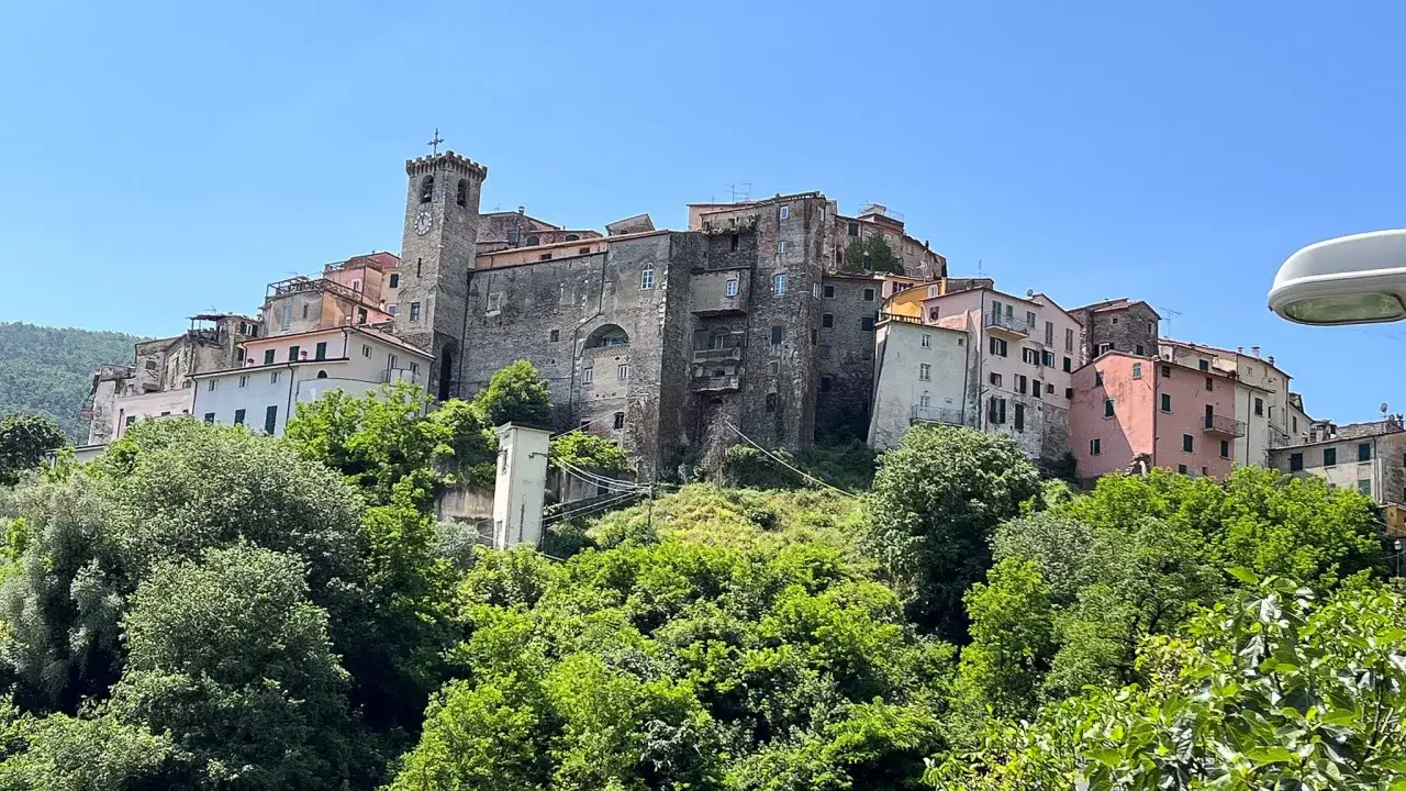 Village d'Ameglia perché sur une colline verdoyante, avec ses maisons colorées et sa tour médiévale sous un ciel bleu.