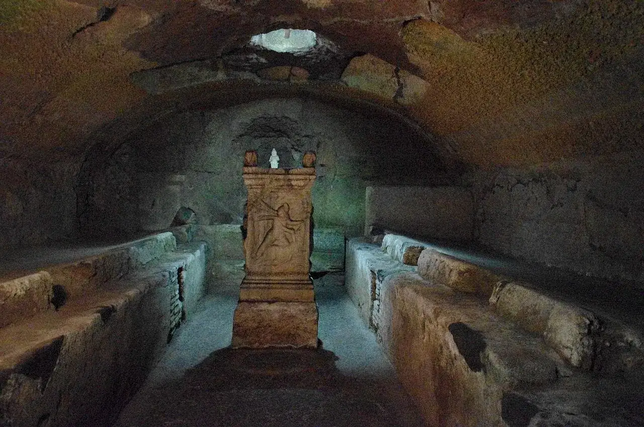 Vestiges souterrains de San Clemente à Rome, avec un autel sculpté au centre et des bancs de pierre de chaque côté.