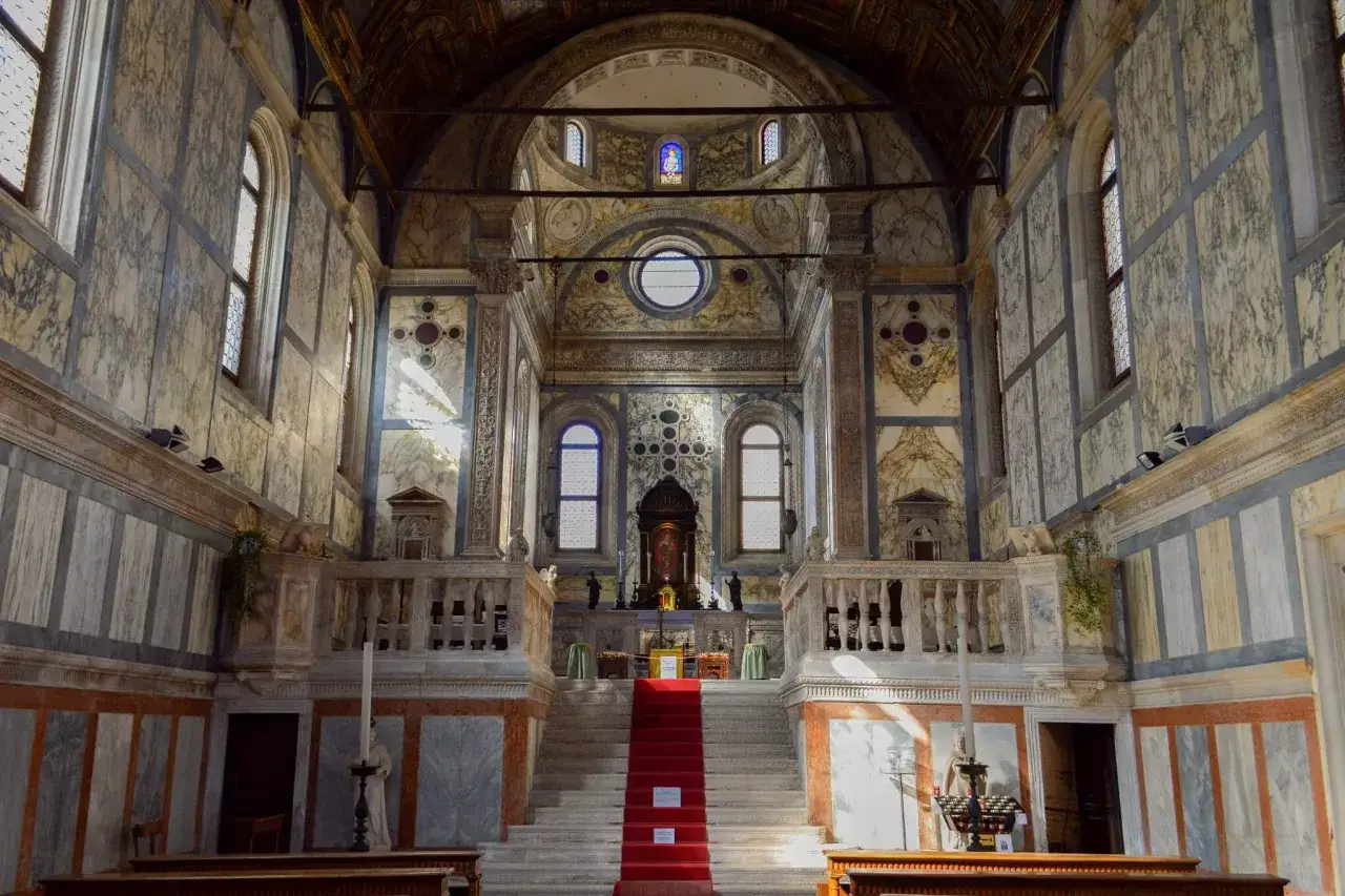 Intérieur d'une église à Venise, avec un escalier rouge menant à l'autel, murs marbrés et vitraux.