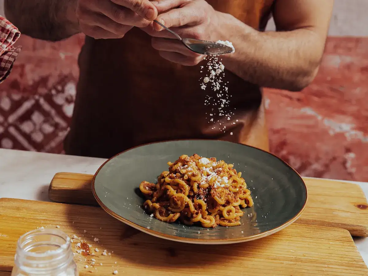 Un chef saupoudre du parmesan sur des pâtes à la bolognaise dans un restaurant. Un plat savoureux qui rappelle Bologne.