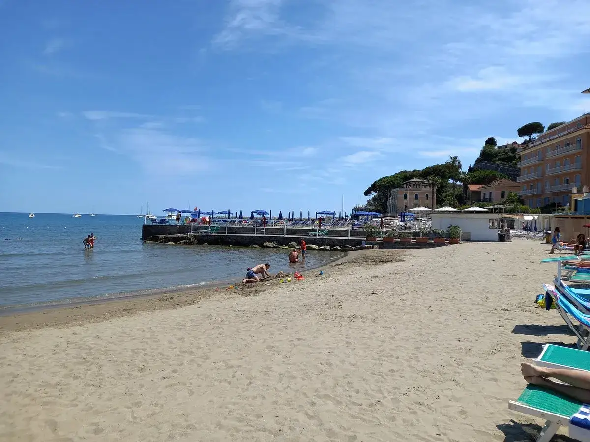 Plage de Diano Marina avec des enfants jouant dans le sable et des parasols bleus.