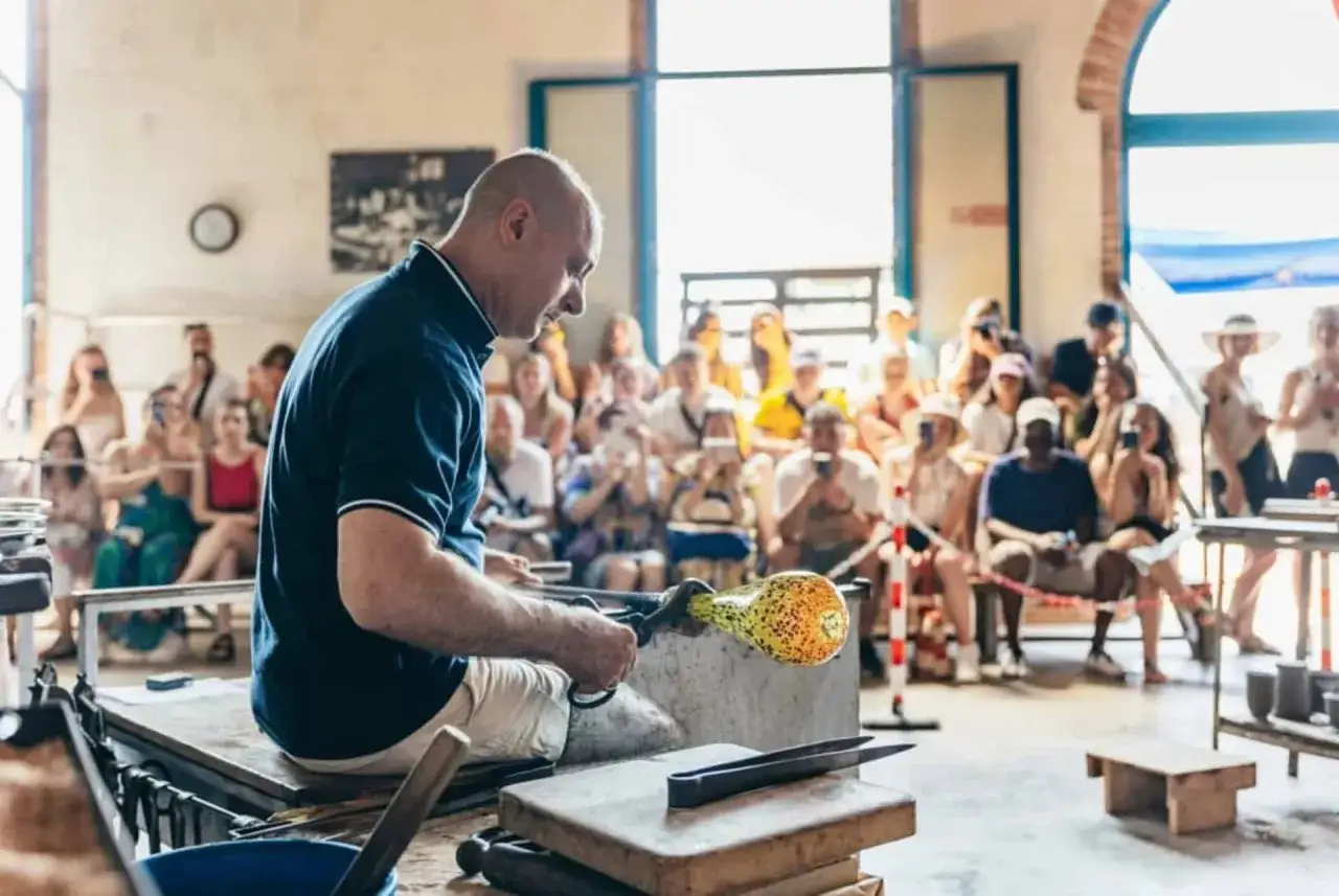 Artisan verrier &agrave; Murano Venise, fa&ccedil;onnant une pi&egrave;ce de verre color&eacute;e devant un public captiv&eacute;.