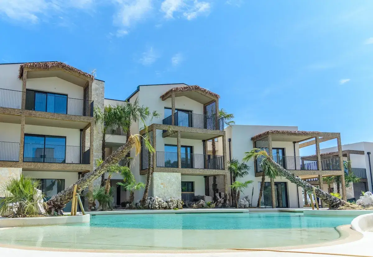 Belle villa à Jesolo avec piscine turquoise et palmiers luxuriants sous un ciel bleu éclatant.