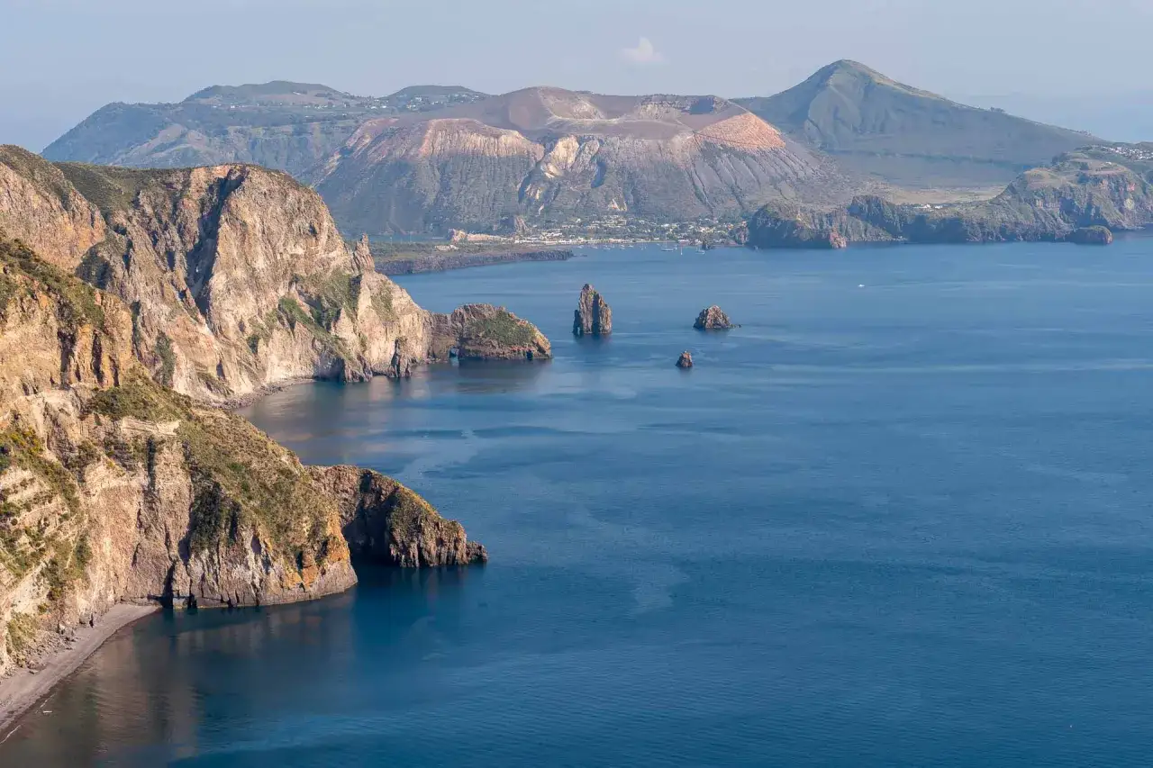 Falaises escarpées et mer bleue près de Lipari, avec un volcan imposant en arrière-plan.