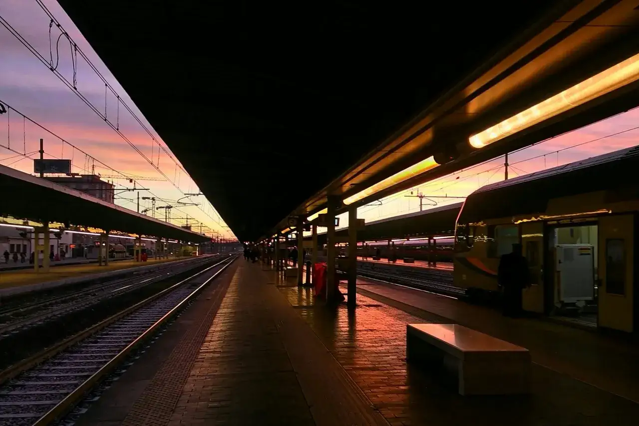 Coucher de soleil sur la gare de Venise Mestre. Les lumi&egrave;res des quais se refl&egrave;tent sur les voies, un train attend patiemment.