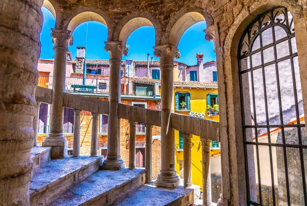 Escalier en colimaçon du Bovolo à Venise, avec ses arches et ses balustrades en pierre, offrant une vue sur les maisons colorées.