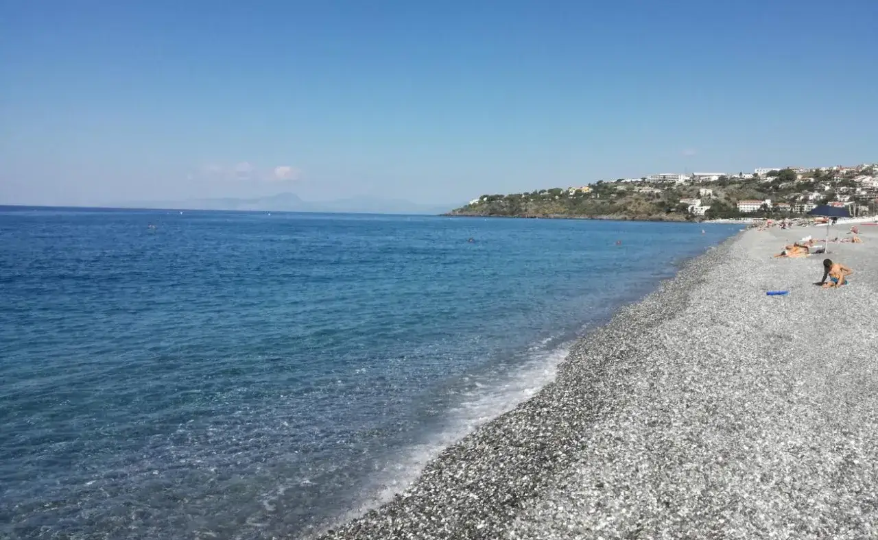 Plage de galets à Scalea, Italie. La mer bleue étincelle sous un ciel clair, avec des maisons perchées sur la colline en arrière-plan.