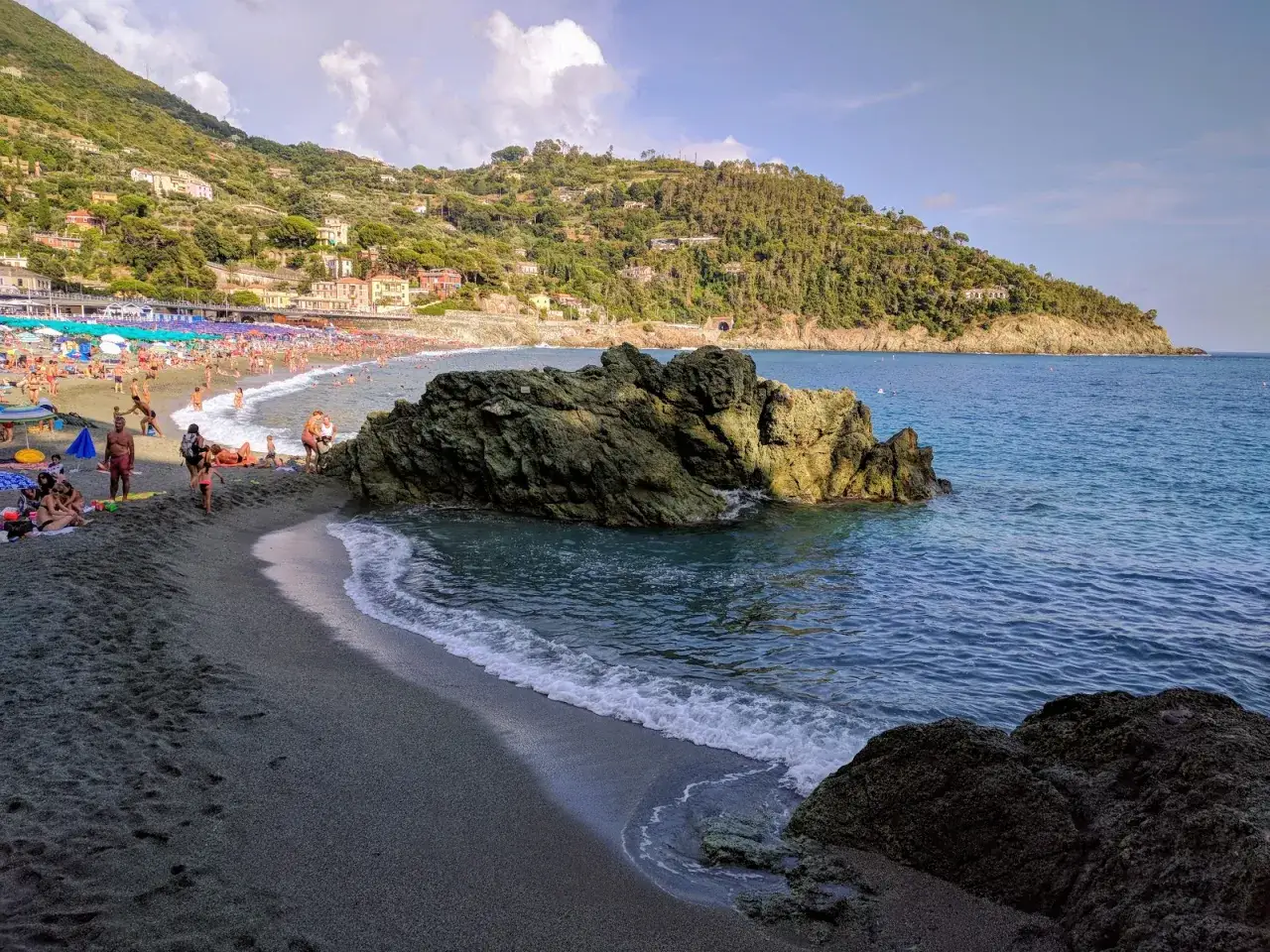 Plage animée à Bonassola, Italie, avec des baigneurs profitant du soleil et de la mer, dominée par une colline verdoyante.