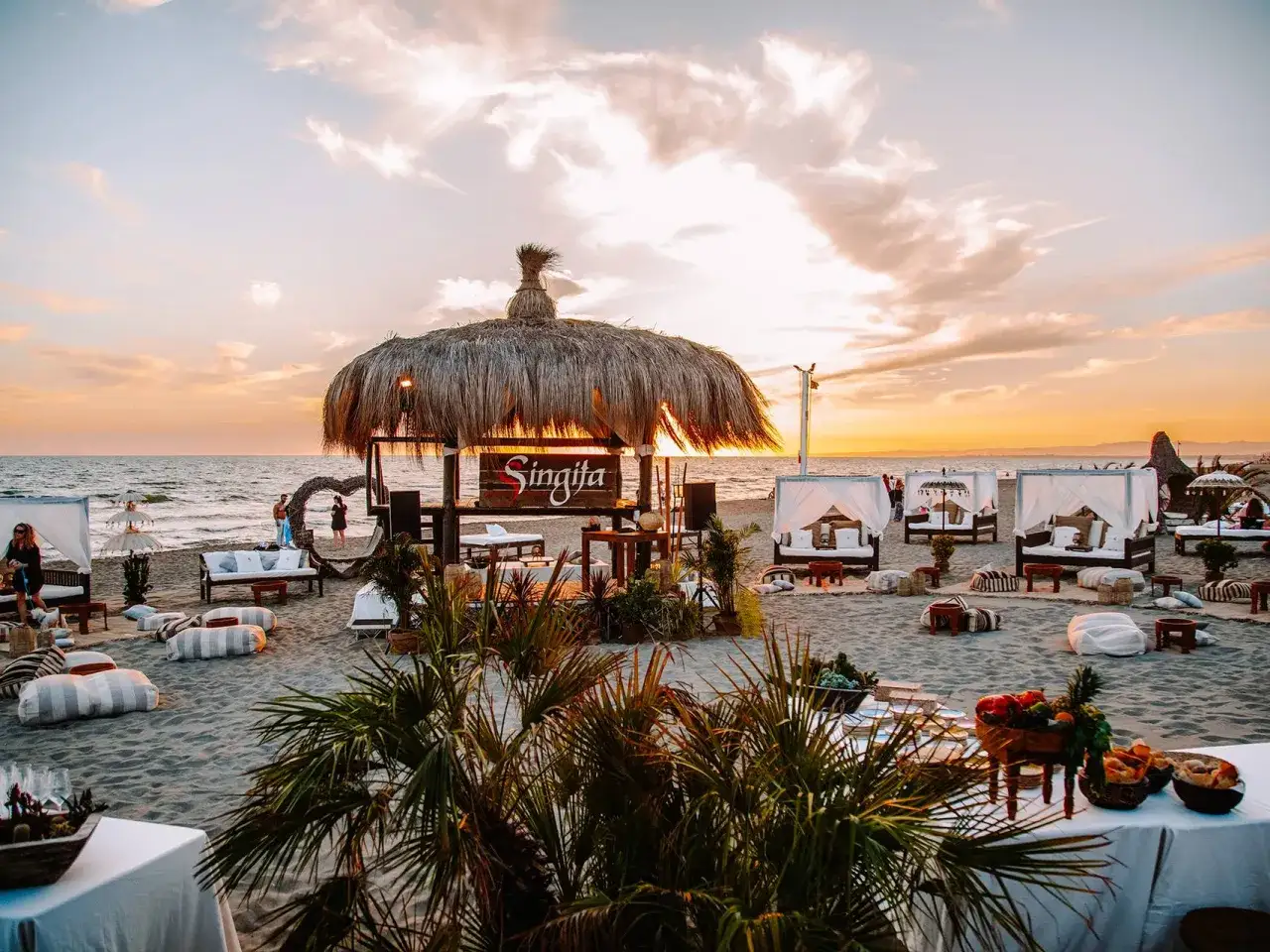 Ambiance de rêve sur la plage au coucher du soleil, avec des tentes blanches, des coussins et le signe 