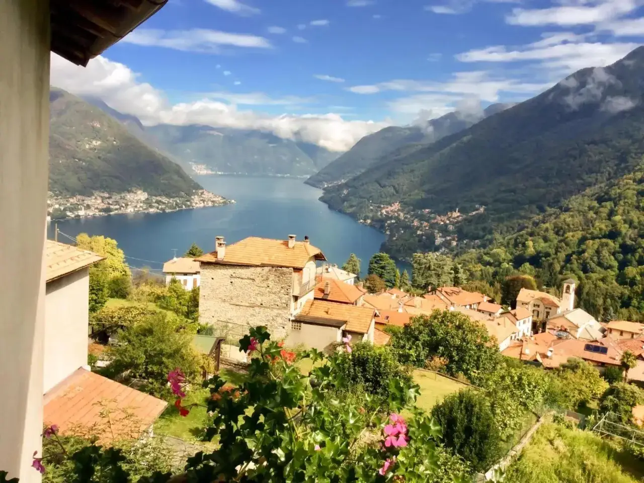 Vue panoramique d'un village pittoresque avec des toits de tuiles rouges, nich&eacute; sur les pentes d'une montagne verdoyante, dominant un lac bleu &eacute;tincelant. Un paysage typique d'une chambre d'h&ocirc;te en Italie du Nord.