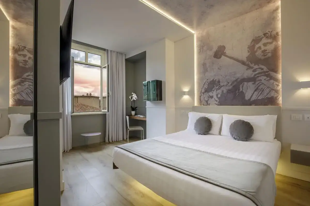 Chambre moderne avec lit douillet, vue sur Rome depuis la fenêtre. Le hotel Regno Rome offre une ambiance unique avec une fresque murale inspirée de l'art antique.
