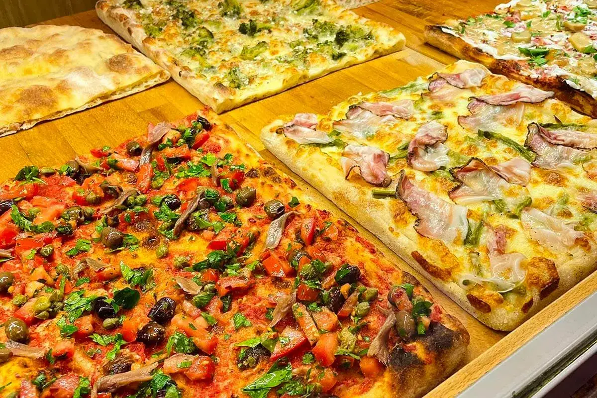 Des pizzas romaines rectangulaires appétissantes, garnies de tomates, olives, anchois et herbes, ou de lardons et asperges. La meilleure pizza à Rome, c'est ici !