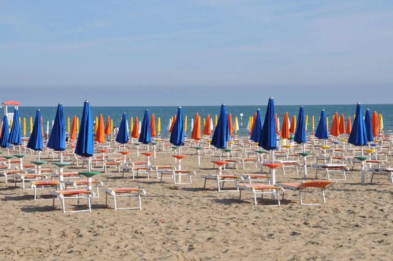 Plage de Lignano, Italie. Rangées de parasols bleus, orange et jaunes, prêts pour les vacanciers.