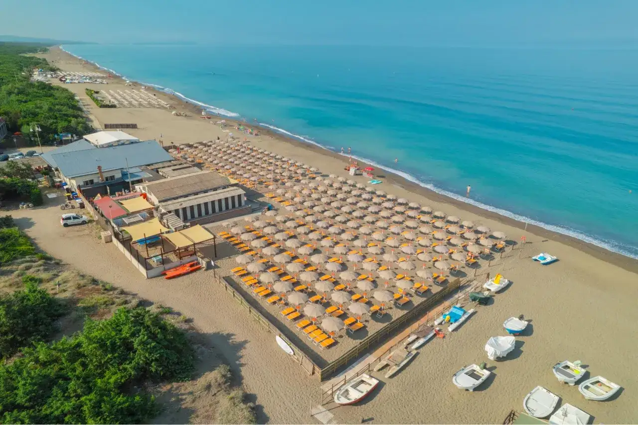 Vue aérienne de la marina di bibbona plage, avec des rangées de parasols orange et des chaises longues sur le sable, face à la mer bleue.