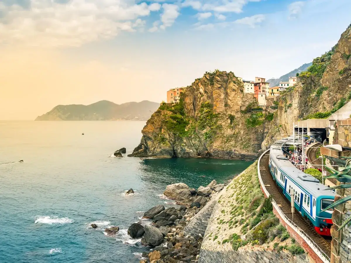 Un train bleu longe la côte italienne, offrant une vue spectaculaire sur la mer et les villages perchés. Une belle façon d'aller en Italie en train.