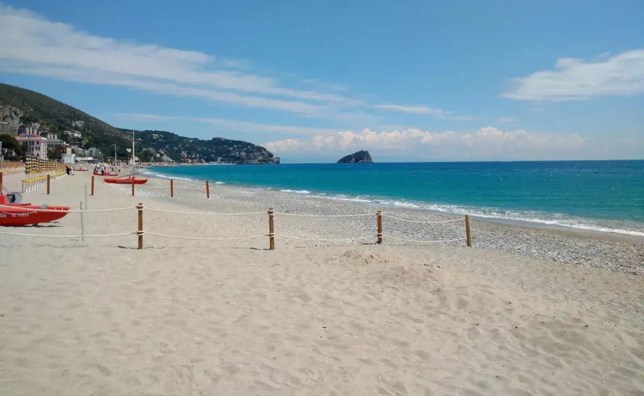 Plage de sable fin &agrave; Spotorno, Italie. Mer turquoise, bateaux de sauvetage rouges et &icirc;lot rocheux au loin.