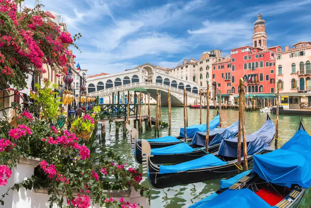 Gondoles bleues attendant les touristes sur le Grand Canal, avec le pont du Rialto en arrière-plan. Idéal pour savoir quand aller à Venise.