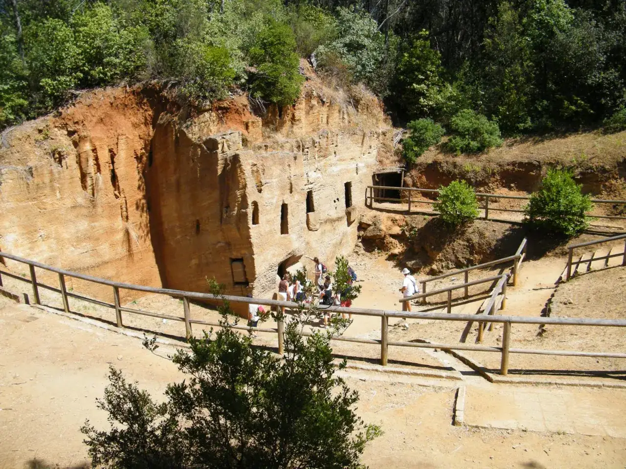 Vestiges archéologiques à Populonia, Italie. Des grottes creusées dans la roche ocre, avec des visiteurs explorant le site.