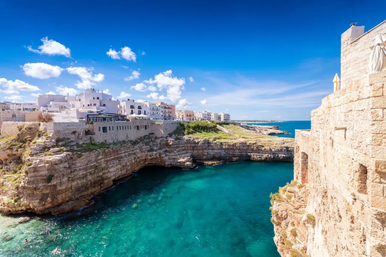 Vue panoramique de Polignano a Mare, les Pouilles. Falaises rocheuses plongeant dans une mer turquoise, maisons blanches perchées sur la côte.