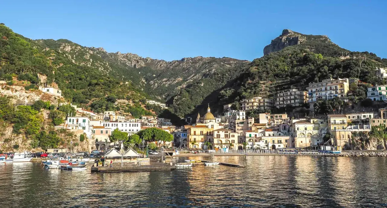 Vue d'un port pittoresque à Cetara, Italie, avec des maisons colorées accrochées à flanc de colline sous un ciel bleu.