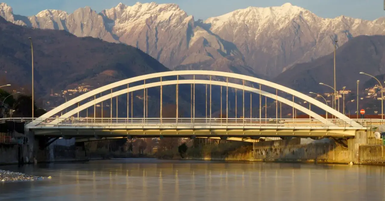 Pont blanc traversant une rivière, avec des montagnes enneigées en arrière-plan. Un paysage typique de Massa, Italie.