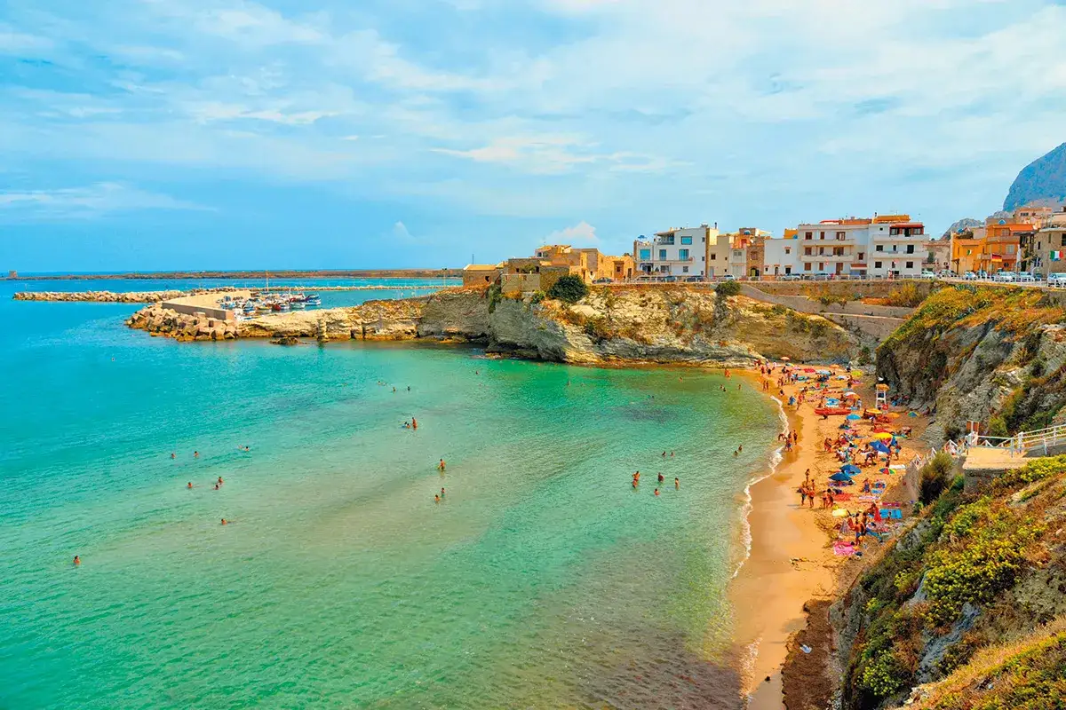 Plage animée à Terrasini, Sicile, avec des eaux turquoise, des maisons colorées perchées sur la falaise et un port de pêche.