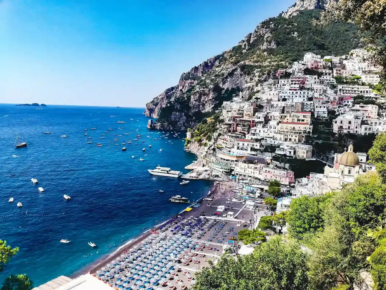 Vue panoramique de Positano, sur la côte amalfitaine, Italie. Des maisons colorées s'accrochent à la falaise, surplombant une plage animée et une mer azur parsemée de bateaux.