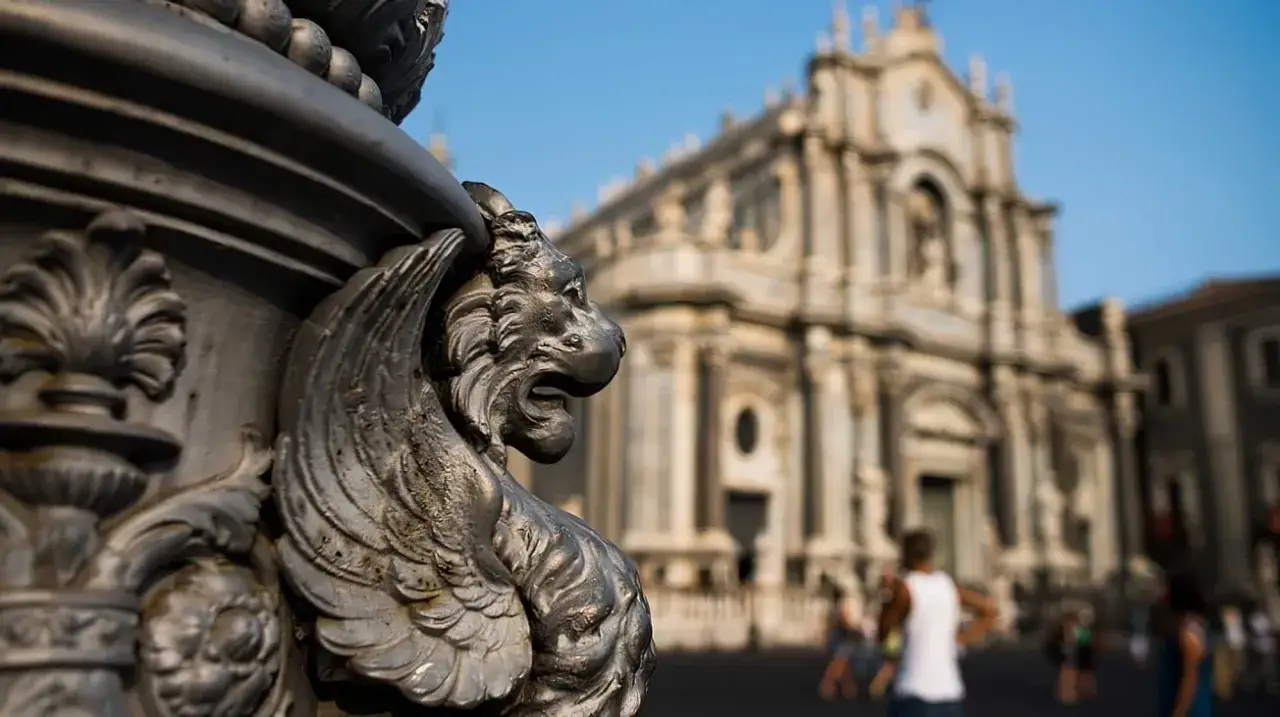 D&eacute;tail d'une gargouille en m&eacute;tal devant la cath&eacute;drale de Catania, Sicile. Le soleil brille sur la place anim&eacute;e.