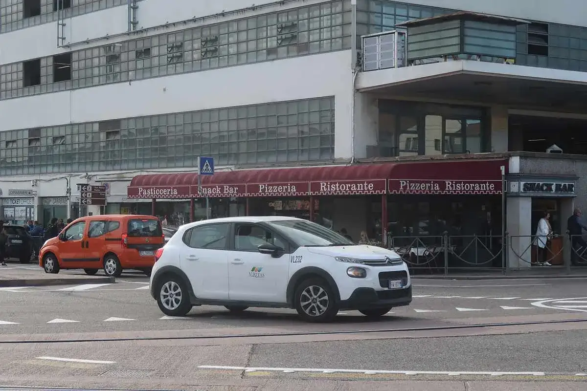 Une voiture blanche circule devant des restaurants et bars. Une autre voiture orange est gar&eacute;e. C'est une sc&egrave;ne de la vie quotidienne, pas vraiment Venise en voiture.