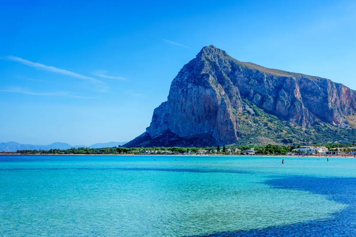 Vue magnifique sur la mer turquoise et la montagne imposante de Capo San Vito, avec une plage animée en arrière-plan.