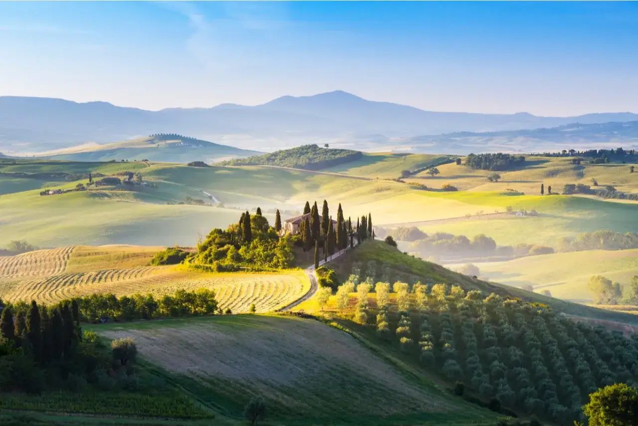 Vue panoramique d'une ferme toscane baign&eacute;e de soleil, avec des collines verdoyantes, des cypr&egrave;s &eacute;lanc&eacute;s et des champs ondulants.