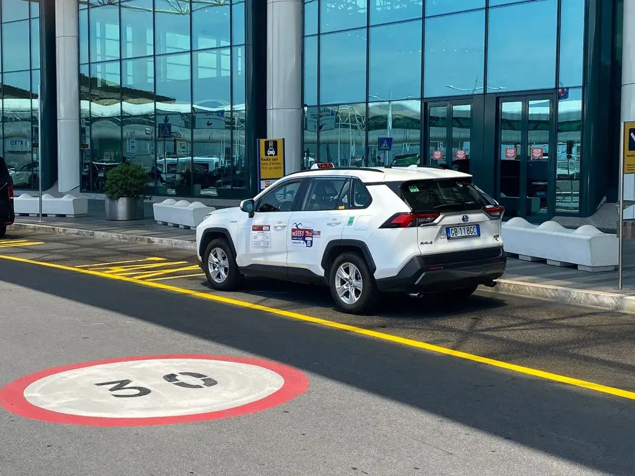 Taxi blanc à l'aéroport de Rome Fiumicino, prêt à vous emmener. Renseignez-vous sur le taxi Rome Fiumicino prix.
