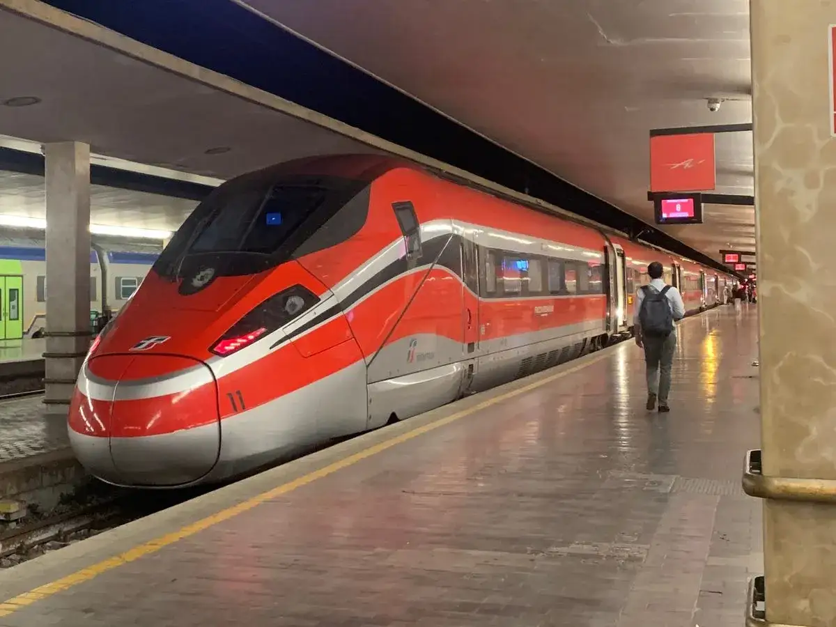 Un train rouge vif pr&ecirc;t &agrave; partir de Rome pour Florence. Un voyageur avec un sac &agrave; dos attend sur le quai.