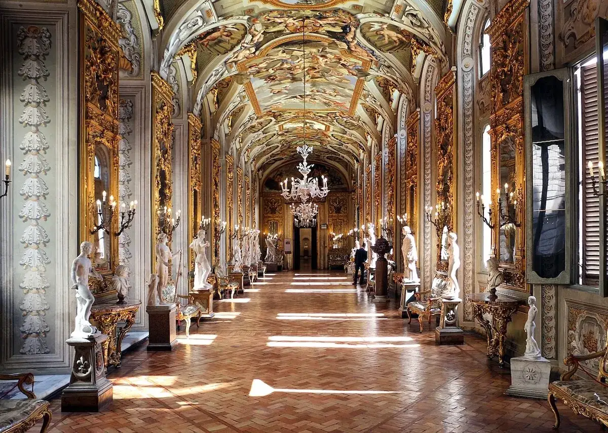 Le Palazzo Doria Pamphilj, un couloir orné de statues, de dorures et de fresques au plafond, baigné de lumière.