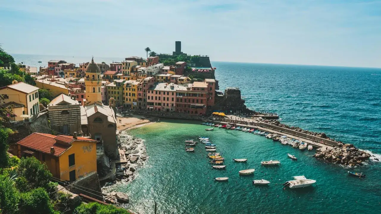 Vue pittoresque de Vernazza, un village coloré accroché à la falaise, où se trouve la Riviera Italienne. Des bateaux flottent dans la baie aux eaux turquoise.