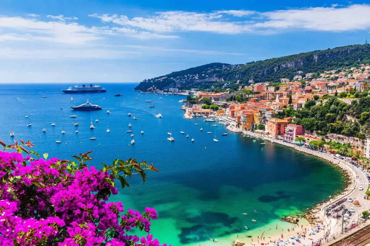 Vue panoramique d'une baie pittoresque avec des maisons colorées, des bateaux et des fleurs roses éclatantes, évoquant la beauté de la finale ligure, Italie.