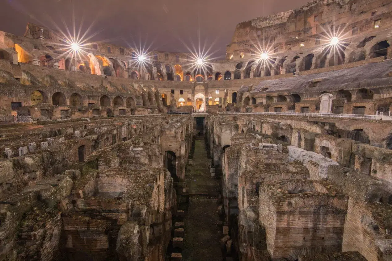 Intérieur du Colisée en Italie la nuit, illuminé par des projecteurs. Les ruines antiques se dressent, témoins silencieux de l'histoire.
