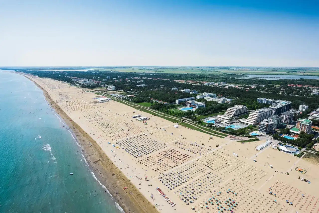 Vue aérienne de la plage de Bibione, Italie, avec des rangées de parasols et de chaises longues, des hôtels et la mer Adriatique.