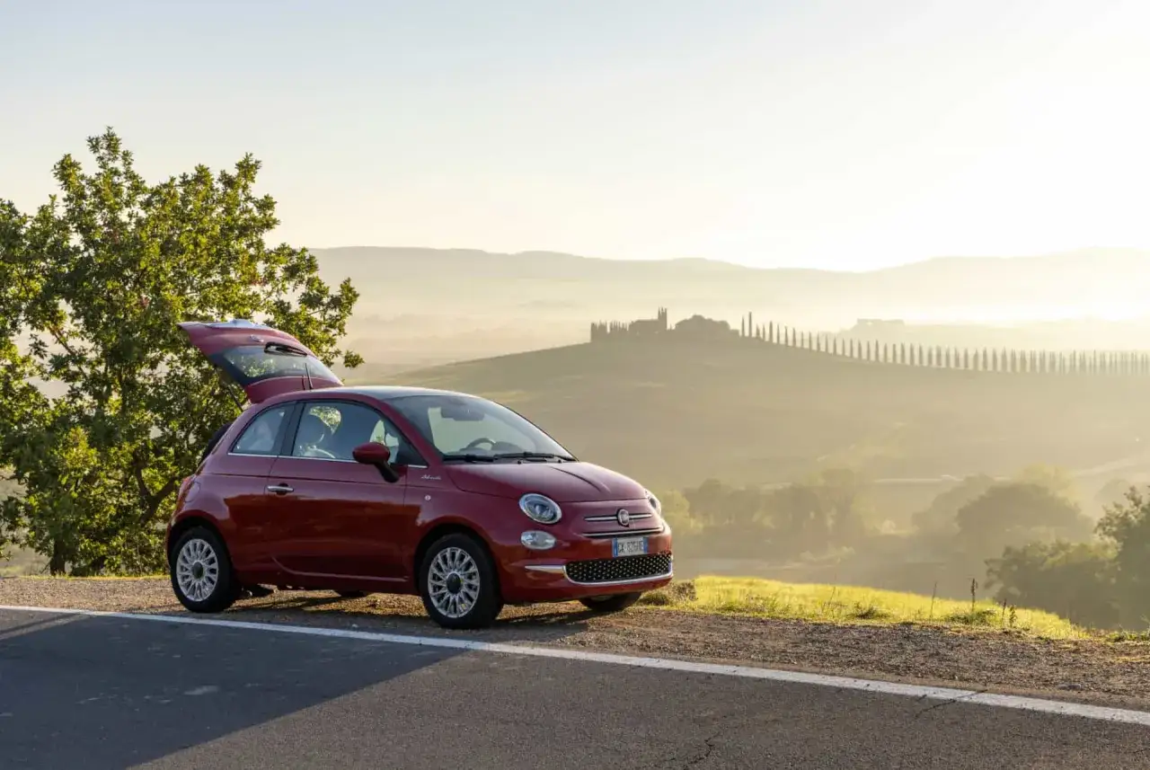 Voiture rouge garée en Italie, paysage toscan. Le prix de cette voiture de rêve est abordable pour une escapade.