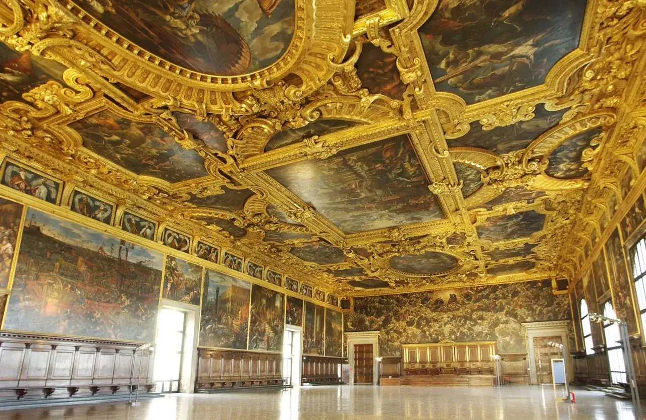 L'opulence dorée du Palais des Doges à Venise se révèle sous un plafond peint et sculpté, ornant une salle majestueuse.
