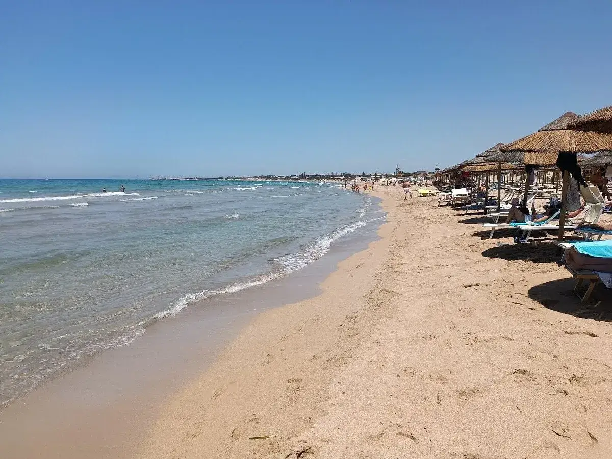 Plage de sable fin à letojanni sicile, avec des parasols de chaume et des transats. La mer est calme et le ciel est bleu.