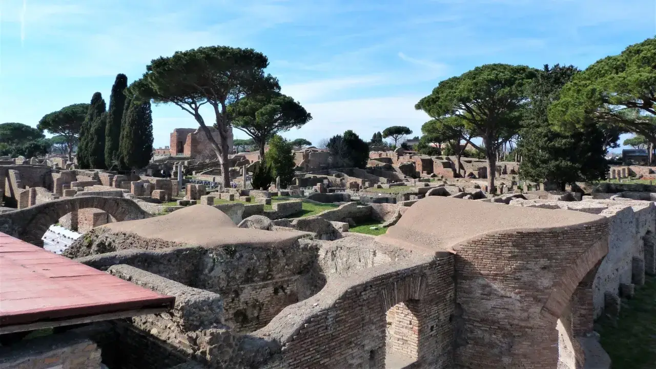 Vestiges de l'ostie antique à Rome, avec des ruines de briques et des pins majestueux sous un ciel bleu.