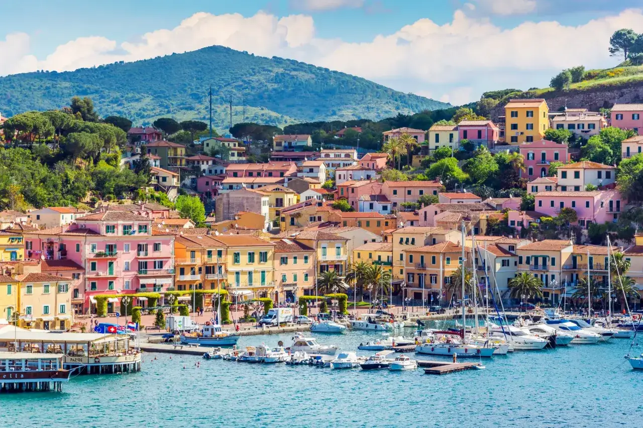 Vue pittoresque de Porto Azzurro, avec ses maisons colorées nichées sur une colline verdoyante surplombant un port animé rempli de voiliers.