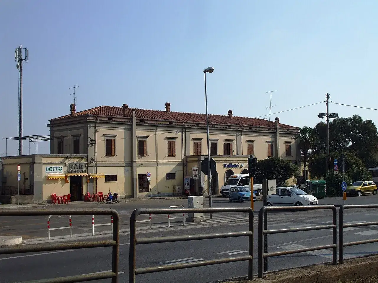 Gare de Velletri, b&acirc;timent beige avec un bar et des tables rouges &agrave; l'ext&eacute;rieur. Des voitures circulent sur la route devant.