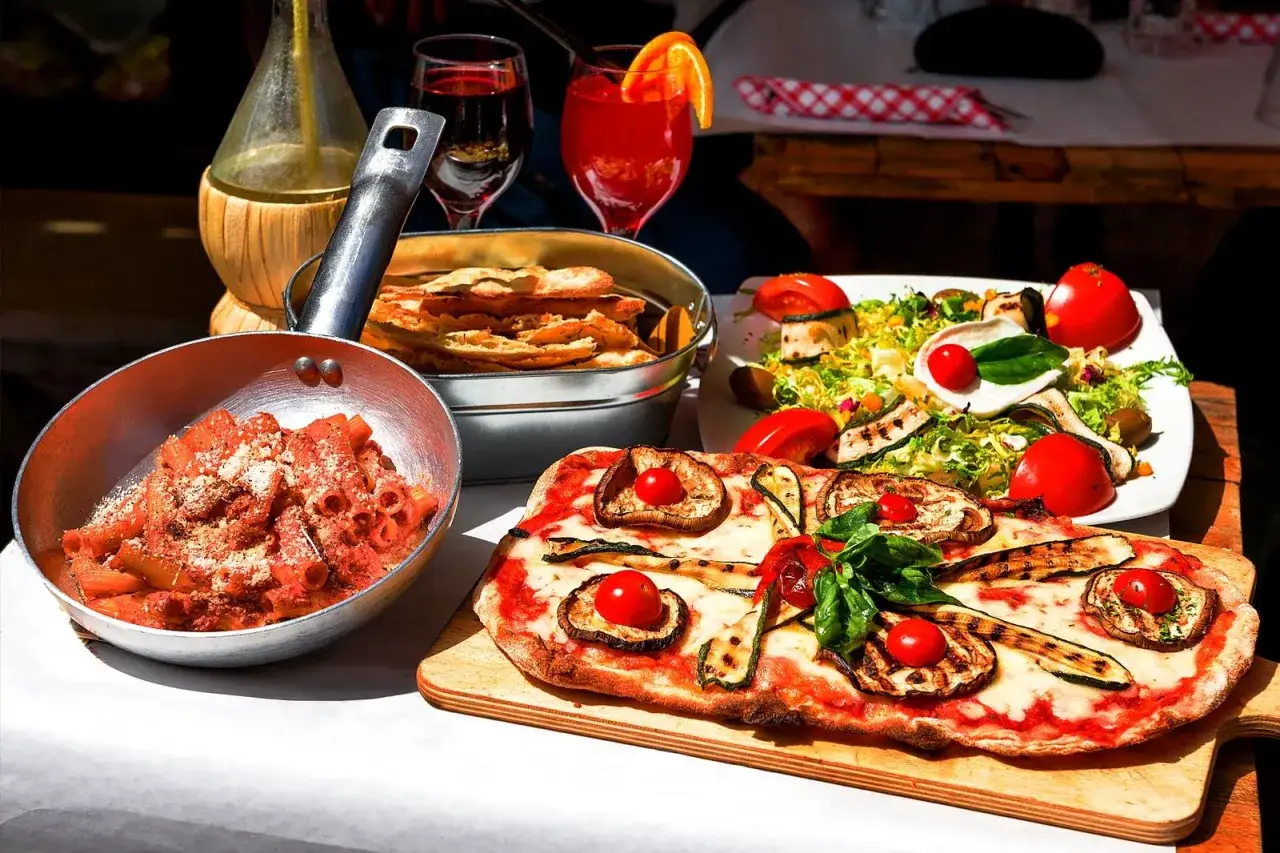 Un festin dans une trattoria à Rome : pâtes, pizza aux légumes grillés, salade fraîche et vin rouge.