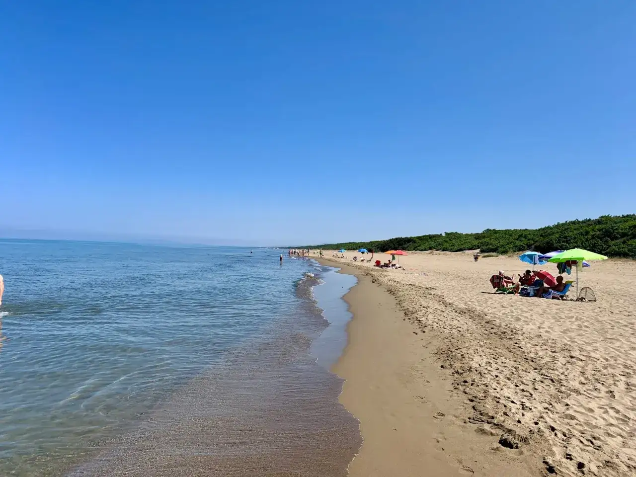 Plage de San Vincenzo en Toscane, avec des baigneurs profitant du soleil sous des parasols colorés. L'eau bleue s'étend à perte de vue.