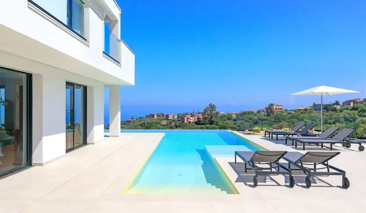 Magnifique gîte en Sicile avec piscine à débordement, chaises longues et vue sur la mer.