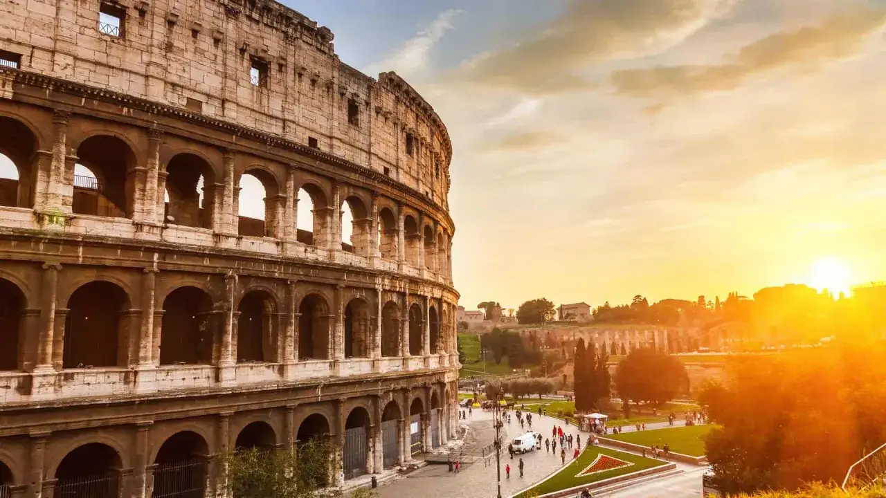 Le Colis&eacute;e de Rome baign&eacute; par le soleil couchant, avec des touristes se promenant sur la place.