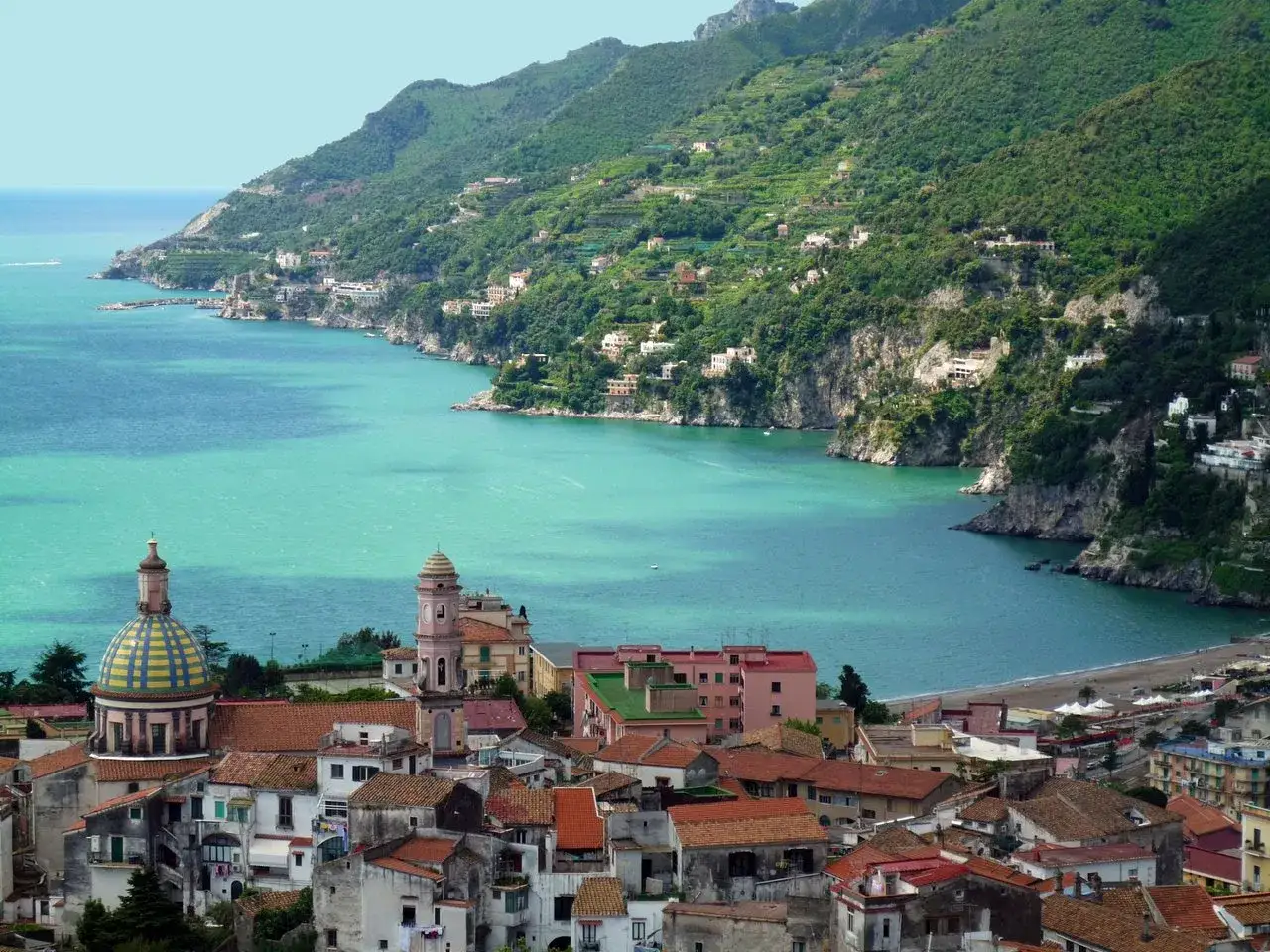 Vue panoramique de Vietri sul Mare, avec ses toits rouges, sa cathédrale et la plage bordant la mer turquoise.